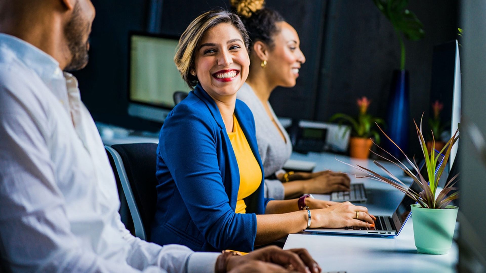 Team working on computers with a woman smiling in conversation